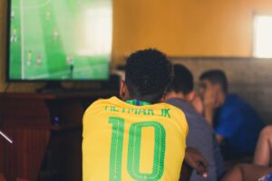 Homem negro assistindo jogo de futebol brasileiro na TV com camisa 10 de Neymar Jr.