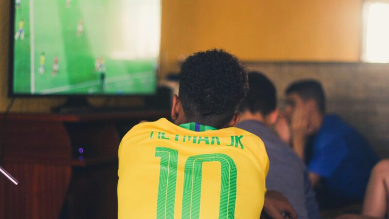 Homem negro assistindo jogo de futebol brasileiro na TV com camisa 10 de Neymar Jr.